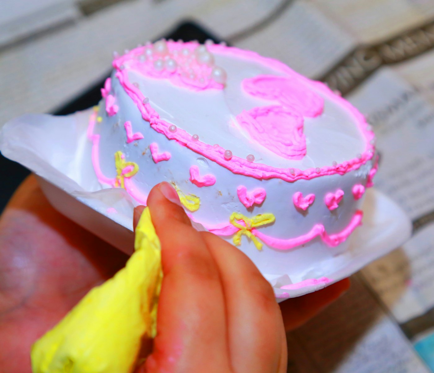A hand piping icing onto a small cake